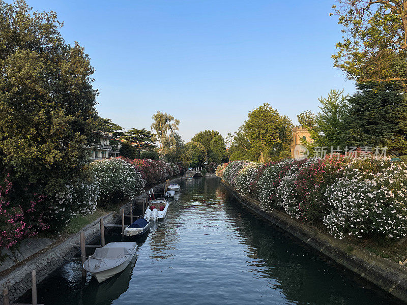 从意大利威尼斯丽都的四喷泉桥(Ponte delle Quattro Fontane)上看运河的特写图片，色彩缤纷的建筑，系泊的船只，湛蓝晴朗的天空，逐渐缩小的视角